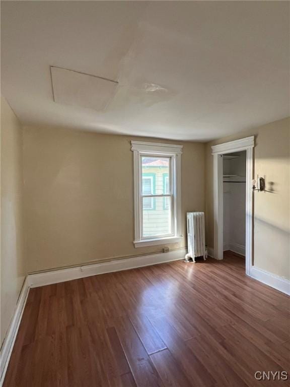 unfurnished bedroom featuring radiator, a closet, wood finished floors, and baseboards
