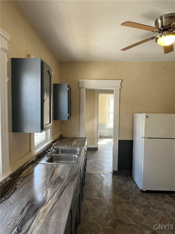 kitchen featuring freestanding refrigerator, stone finish flooring, a wainscoted wall, ceiling fan, and a sink