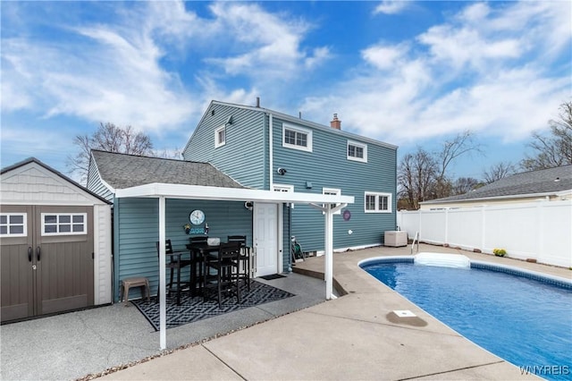 rear view of house featuring fence, an outbuilding, a fenced in pool, a storage shed, and a patio area