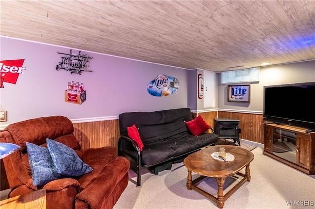 living area with a wood stove, wooden ceiling, wooden walls, a wainscoted wall, and light carpet