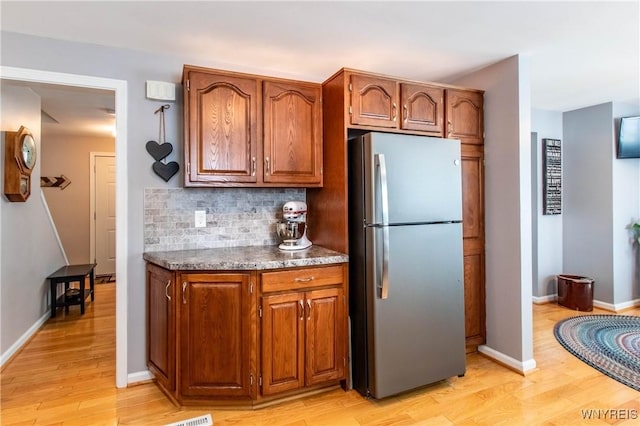 kitchen featuring light wood-style floors, brown cabinetry, backsplash, dark countertops, and freestanding refrigerator