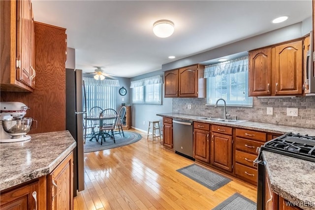 kitchen with appliances with stainless steel finishes, ceiling fan, brown cabinetry, and a sink