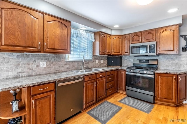 kitchen featuring brown cabinets, light wood-style floors, appliances with stainless steel finishes, and a sink