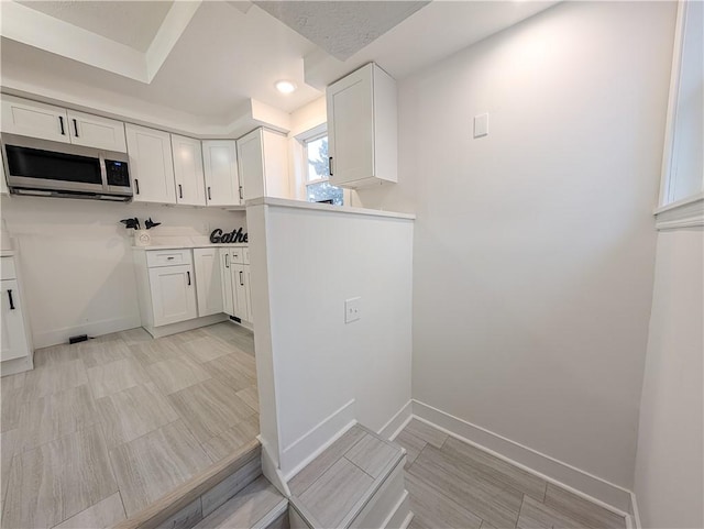 kitchen featuring stainless steel microwave, white cabinetry, and baseboards