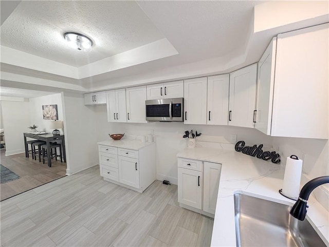 kitchen featuring stainless steel microwave, a sink, white cabinetry, a textured ceiling, and a tray ceiling