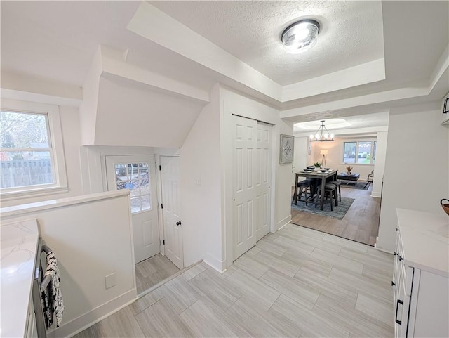 hallway with an inviting chandelier, a textured ceiling, a tray ceiling, and baseboards