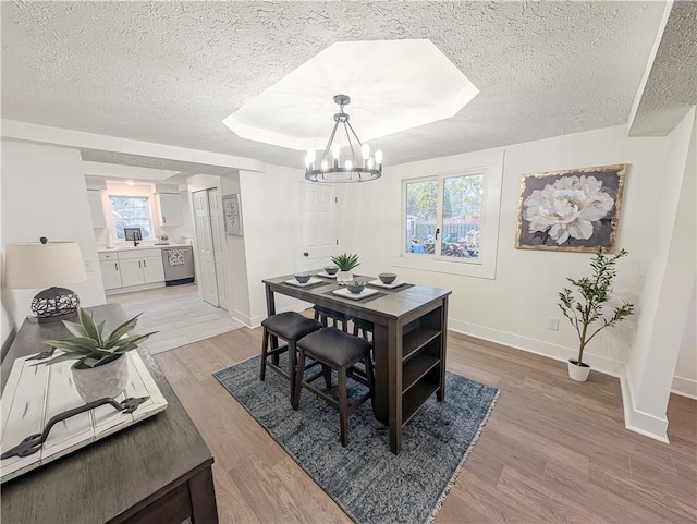 dining area with light wood-type flooring, a textured ceiling, an inviting chandelier, and baseboards