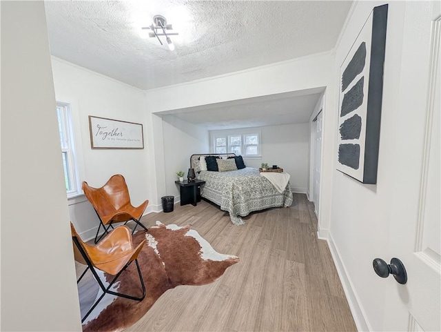 bedroom with baseboards, wood finished floors, a textured ceiling, and ornamental molding