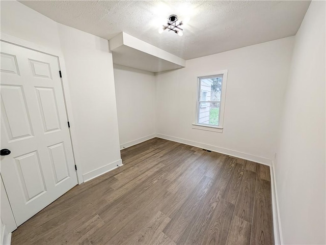 unfurnished room featuring a textured ceiling, wood finished floors, visible vents, and baseboards