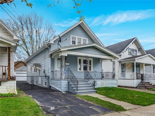 view of front of property with a porch, a detached garage, a front lawn, and a gate
