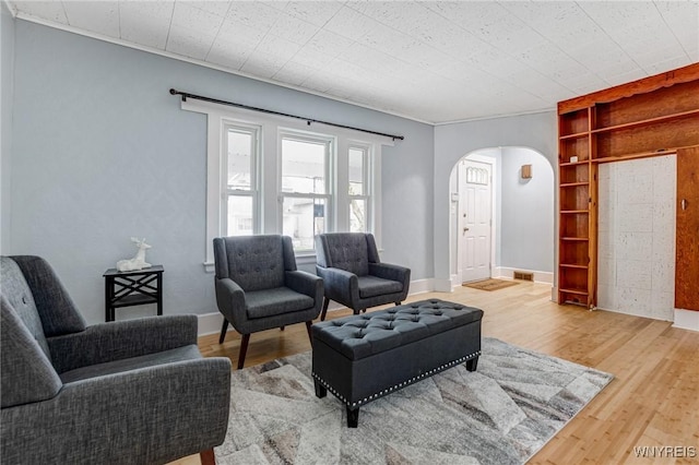 living area with wood finished floors, baseboards, built in features, and arched walkways