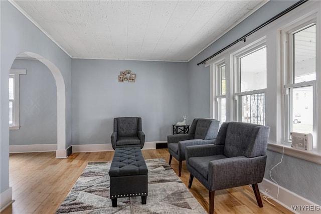 living area with wood finished floors, cooling unit, ornamental molding, and arched walkways