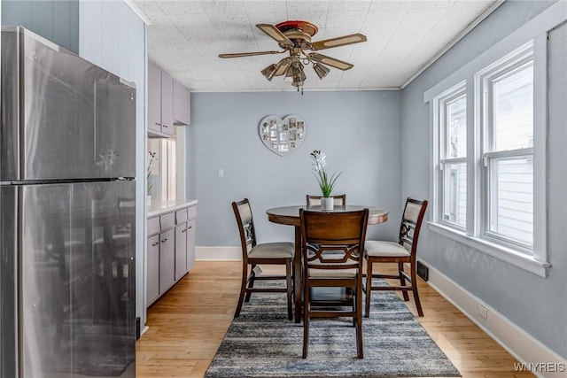 dining area featuring light wood-style floors, a ceiling fan, and baseboards