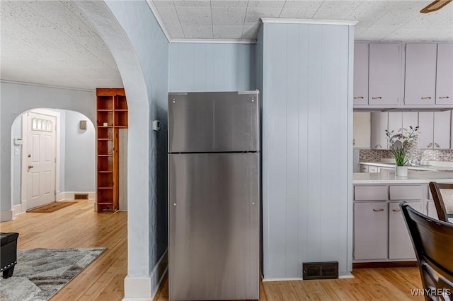 kitchen with light wood finished floors, visible vents, light countertops, arched walkways, and freestanding refrigerator