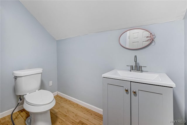 half bath featuring wood finished floors, vaulted ceiling, toilet, vanity, and baseboards