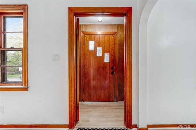 hall featuring baseboards, arched walkways, a healthy amount of sunlight, and wood finished floors