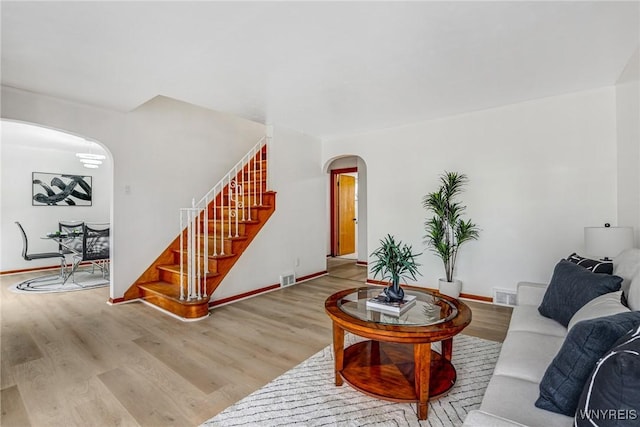 living room featuring stairs, visible vents, baseboards, arched walkways, and wood finished floors