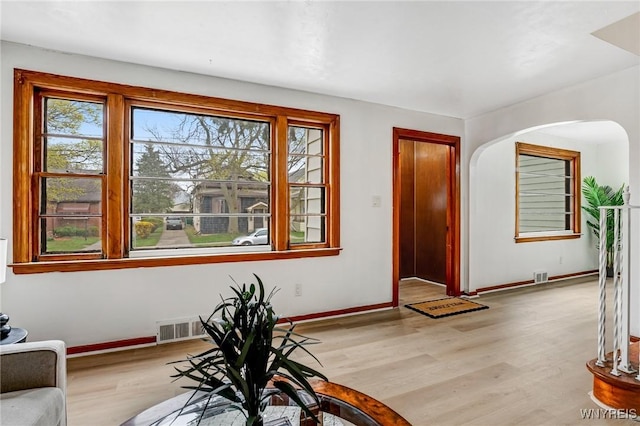 foyer with baseboards, arched walkways, a wealth of natural light, and light wood-style flooring