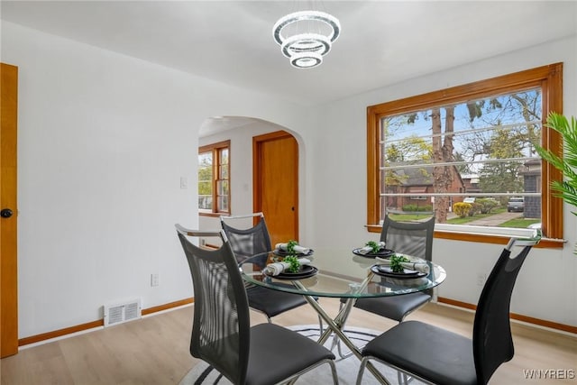 dining room featuring arched walkways, an inviting chandelier, wood finished floors, baseboards, and visible vents