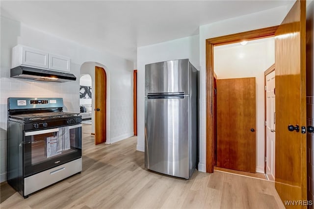 kitchen featuring appliances with stainless steel finishes, light wood-style floors, baseboards, arched walkways, and under cabinet range hood