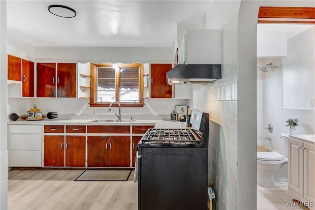 kitchen with tile walls, a sink, under cabinet range hood, range with gas cooktop, and light countertops