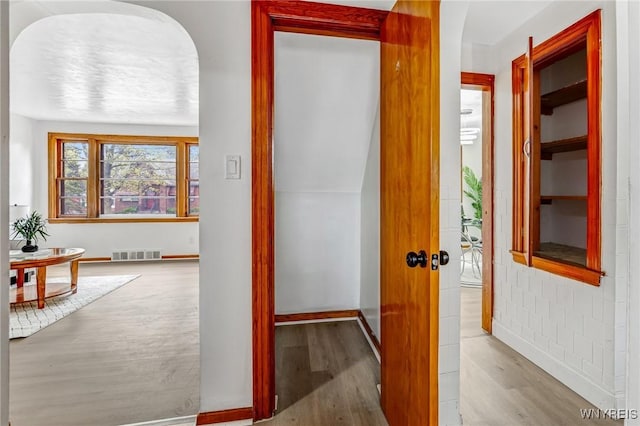 hallway featuring baseboards, visible vents, wood finished floors, and arched walkways