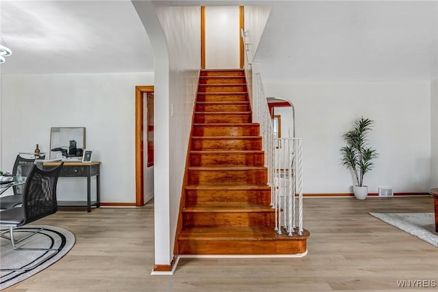 stairway with baseboards, arched walkways, and wood finished floors