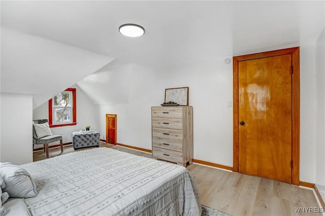 bedroom featuring light wood finished floors, lofted ceiling, and baseboards