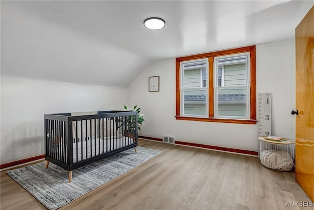 bedroom with lofted ceiling, wood finished floors, visible vents, and baseboards