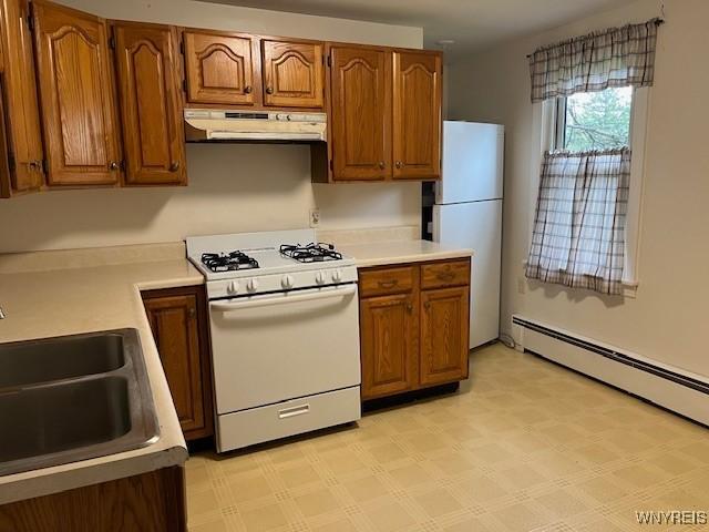 kitchen with brown cabinetry, a sink, under cabinet range hood, and white appliances