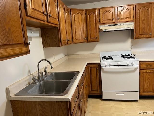 kitchen with under cabinet range hood, light countertops, brown cabinets, a sink, and white gas stove