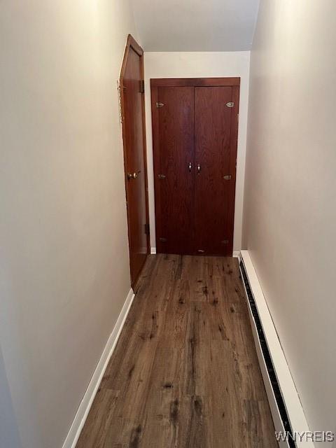 hallway featuring wood finished floors, a baseboard heating unit, and baseboards