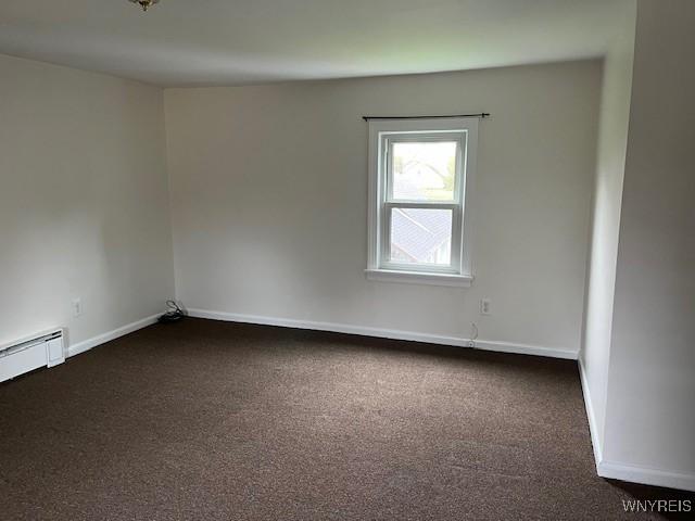 empty room featuring a baseboard heating unit, dark colored carpet, and baseboards