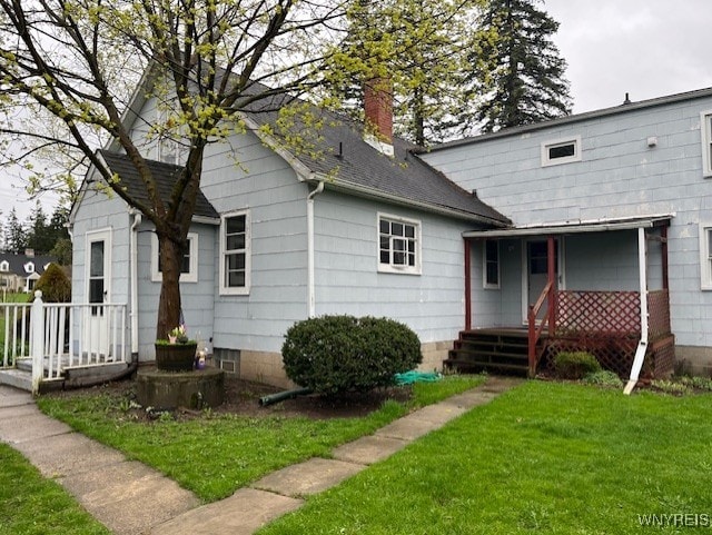 back of house featuring a porch, a yard, a shingled roof, and a chimney