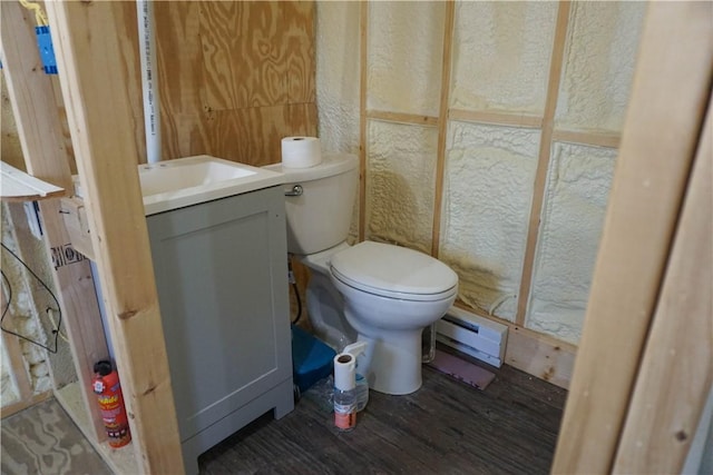 half bath featuring vanity, wood finished floors, toilet, and a baseboard heating unit