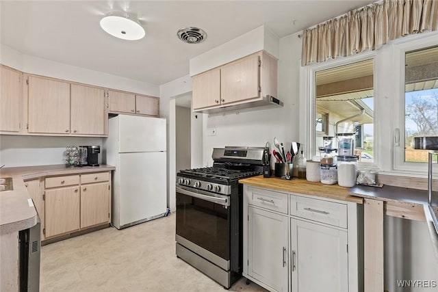 kitchen featuring stainless steel gas range, light countertops, freestanding refrigerator, and light brown cabinets