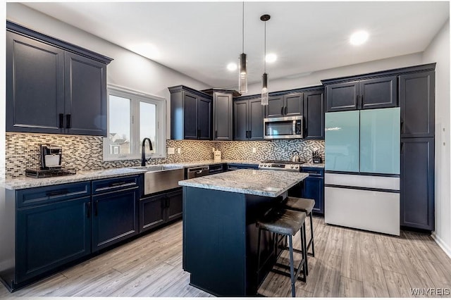 kitchen with fridge, stainless steel microwave, light stone countertops, a sink, and a kitchen bar