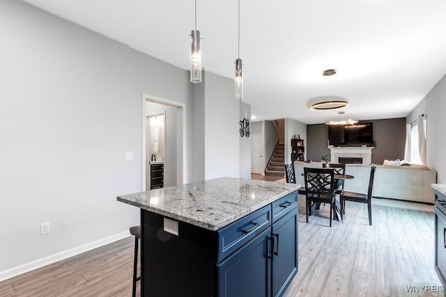 kitchen featuring blue cabinetry, decorative light fixtures, light wood finished floors, a fireplace, and open floor plan