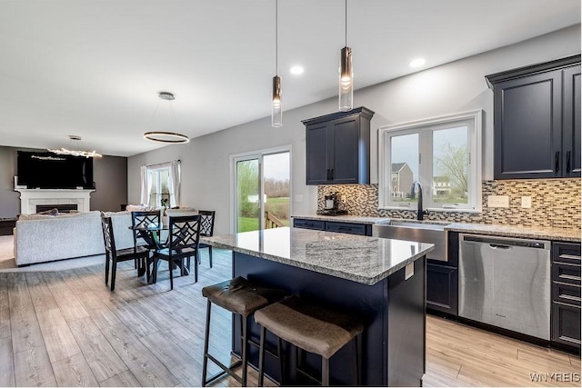 kitchen featuring light stone countertops, stainless steel dishwasher, decorative backsplash, a sink, and open floor plan