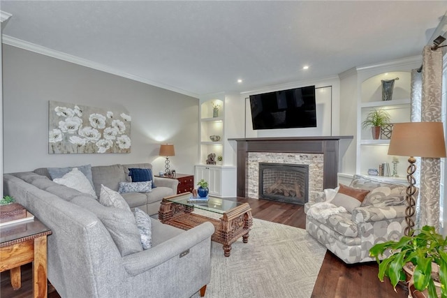 living area with recessed lighting, wood finished floors, built in features, ornamental molding, and a stone fireplace