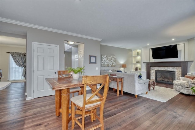 dining space with wood finished floors, built in shelves, a stone fireplace, and crown molding