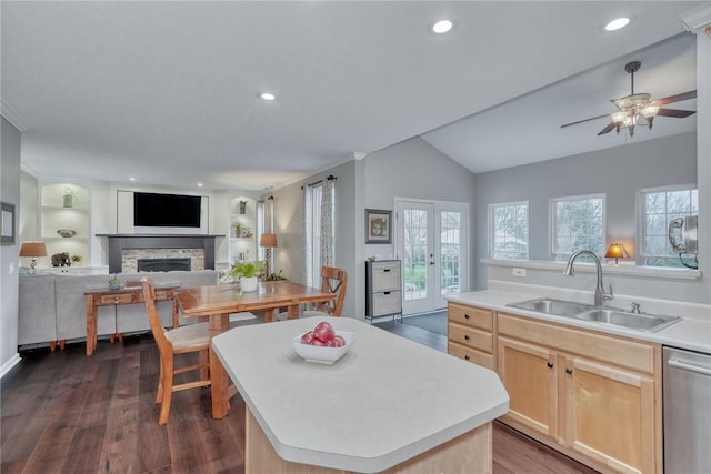 kitchen featuring a sink, a fireplace, light brown cabinetry, vaulted ceiling, and stainless steel dishwasher