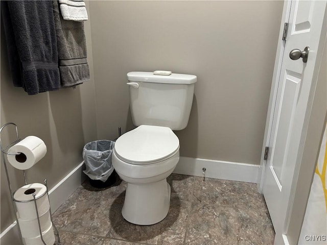 bathroom with toilet, stone finish flooring, and baseboards
