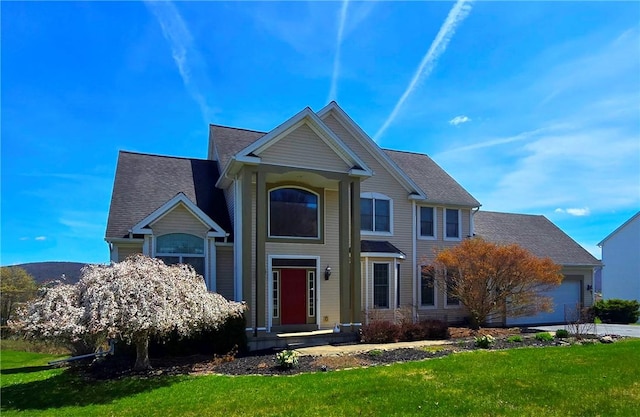 traditional-style house with a shingled roof, a front yard, concrete driveway, and an attached garage