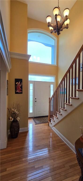 foyer with hardwood / wood-style floors, baseboards, a towering ceiling, a notable chandelier, and stairs