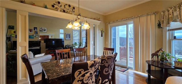 dining area with ornamental molding, an inviting chandelier, a wealth of natural light, and wood finished floors