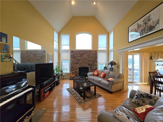 living area with high vaulted ceiling, light wood-style floors, a healthy amount of sunlight, and a fireplace