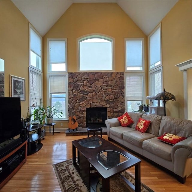 living room with high vaulted ceiling, a stone fireplace, and light wood-style flooring