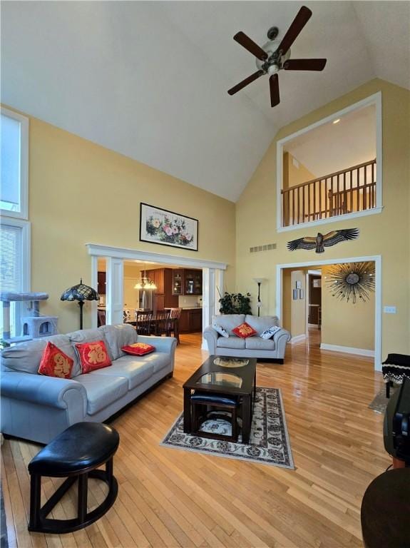living room featuring visible vents, baseboards, wood-type flooring, a ceiling fan, and high vaulted ceiling