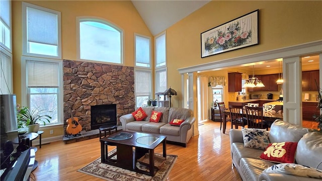 living area with plenty of natural light, high vaulted ceiling, a stone fireplace, and a notable chandelier